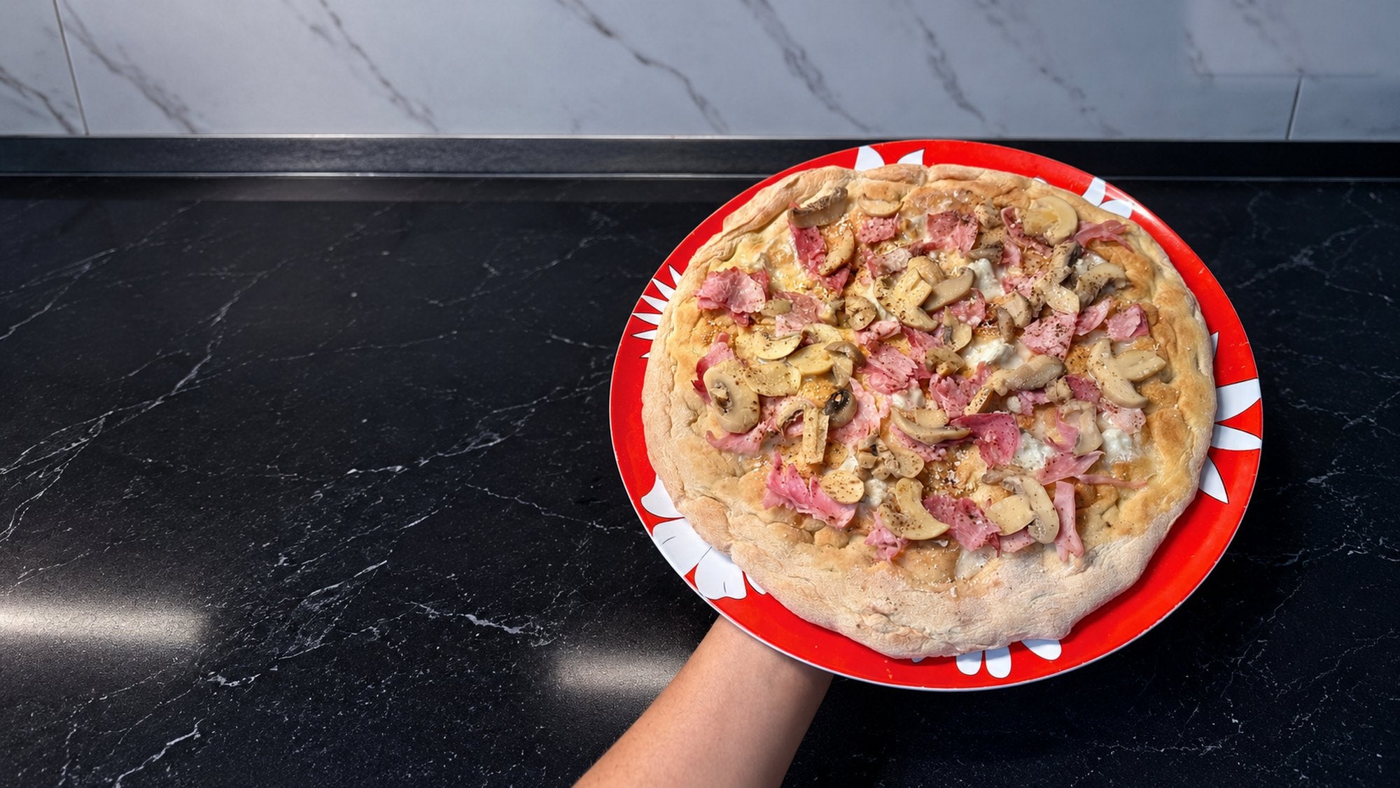 Una pizza con funghi e prosciutto servita su un piatto rosso